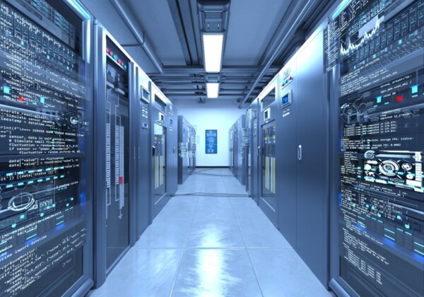 Data center corridor with rows of server racks and blue-tinged lighting, code and dashboards displayed on panels nearby.